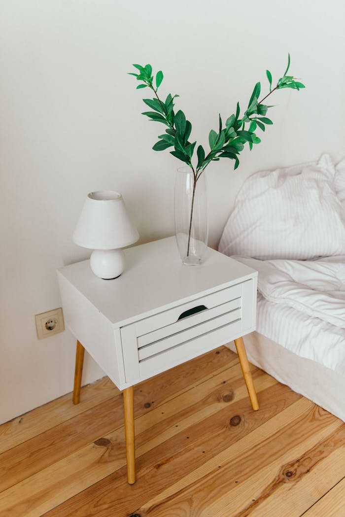 A stylish bedroom showcasing a white nightstand with a vase and lamp, perfect for modern interior design inspiration.